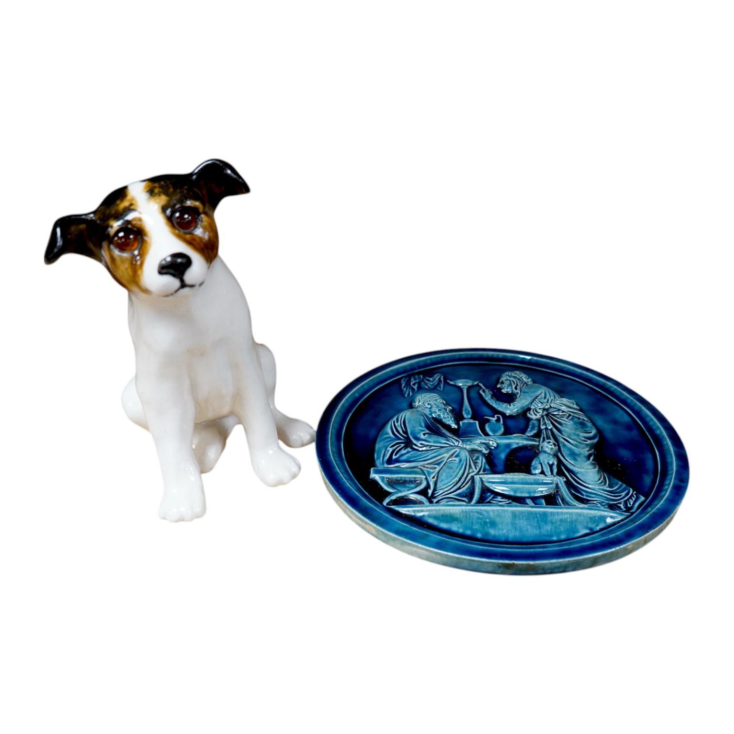 A Copenhagen P Ipson circular glazed plaque, representing Winter/Ages of Man, and a J. Winstanley pottery seated dog with glass eyes, largest 27cm in diameter. Condition - good, the right ear of the Winstanley dog has be